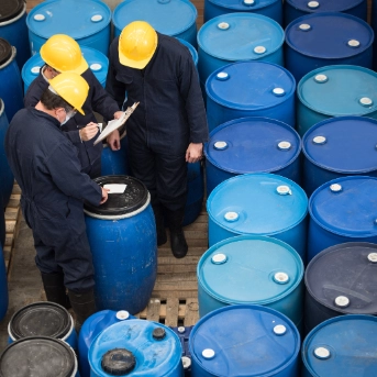 Three men inspecting chemical drums