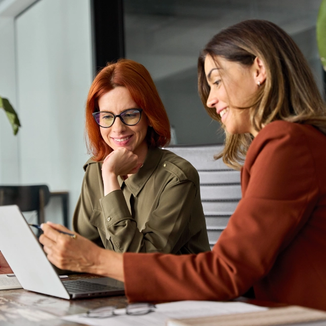 Two smiling young women reviewing work on a laptop